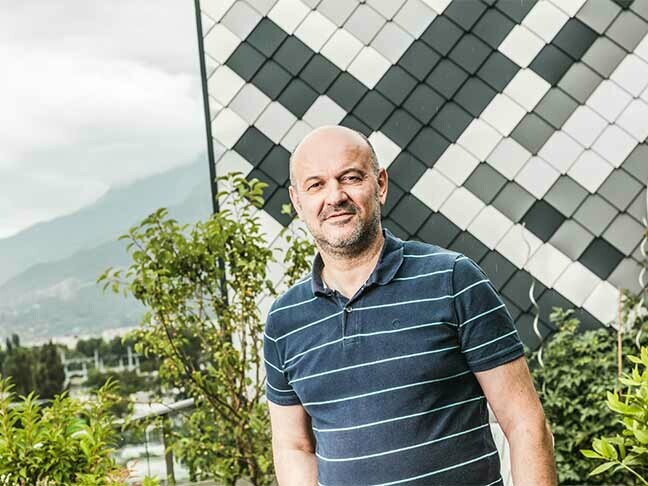 Portrait de l'artisant Patrick Gaide devant son bâtiment prestigieux en losange de façade en aluminium PREFA vêtu d'un polo foncé