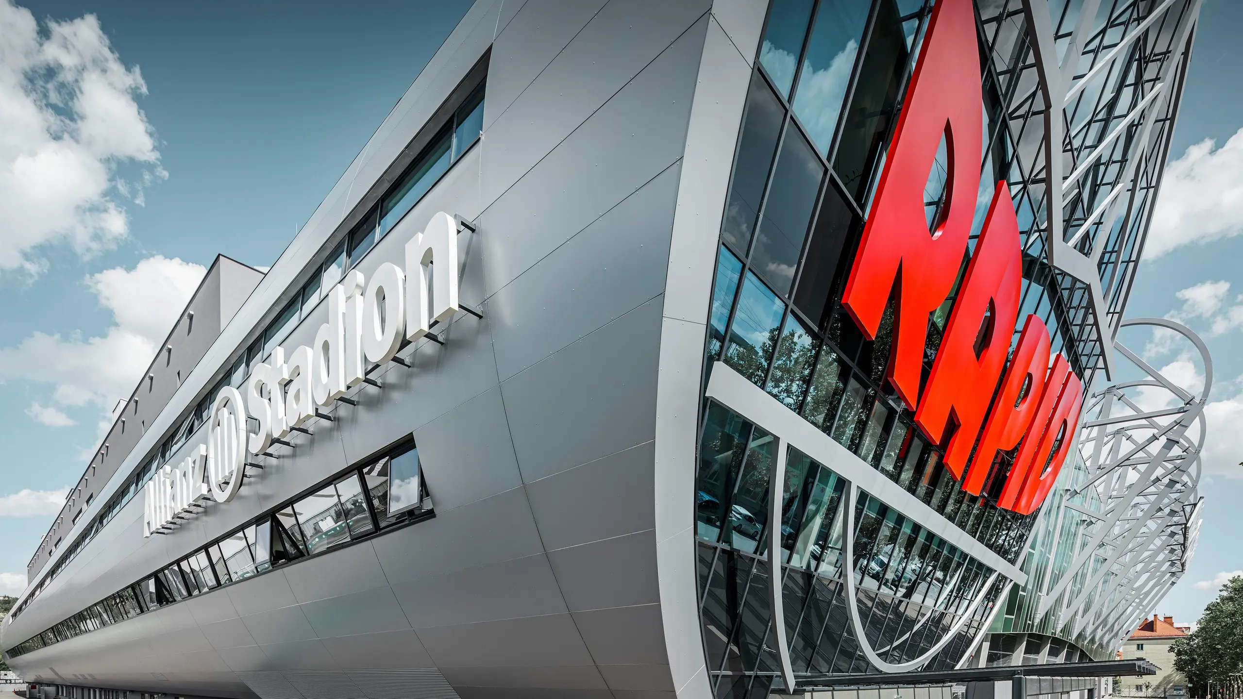 Nahaufnahme der Fassade des Allianz Stadions, Heimat des SK Rapid Wien. Die eindrucksvolle Röhre im Eingangsbereich präsentiert die PREFA Aluminium Verbundplatten in Silbermetallic. Der Blickwinkel unterstreicht die moderne Architektur. Durch den strahlend roten RAPID-Schriftzug und die klare Linienführung der silbernen Platten erhält die Röhre eine visuell beeindruckende Dynamik und Ästhetik. Auf diese Weise wird bereits beim Gang zum Stadion bei allen Fußball-Fans Leidenschaft entfacht.