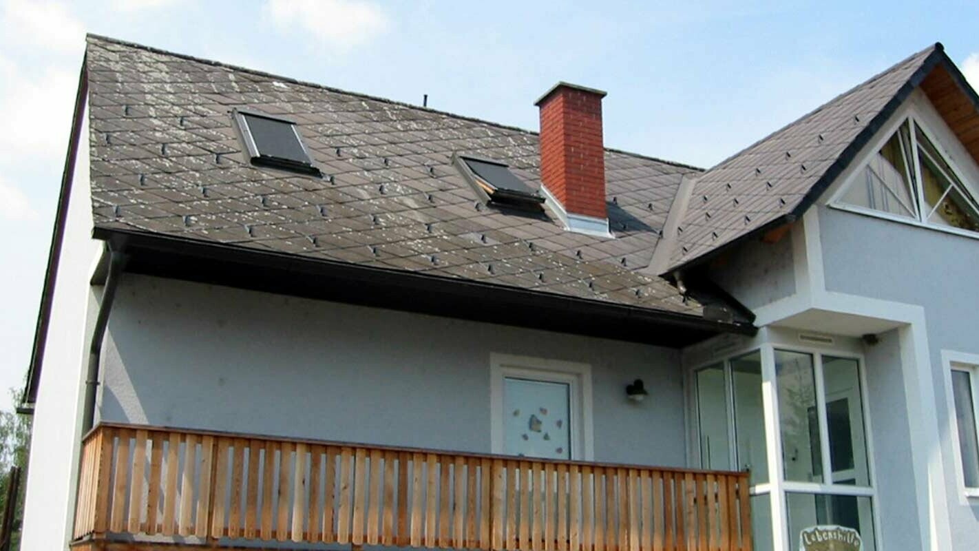 Einfamilienhaus mit Satteldach, blauer Fassade und Schornstein mit Ziegeln gemauert mit altem Dach, bereit für die Dachsanierung