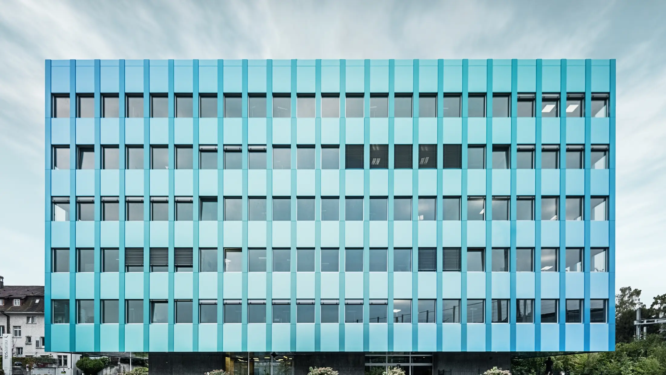 Frontale Ansicht des Wielandhauses in Aarau mit vielen Fenstern und einer blau-grünen PREFABOND Aluminiuim Verbundplatten-Fassade von PREFA. Die Fassade schimmert in blau/grün durch das eigene Beschichtungsverfahren.