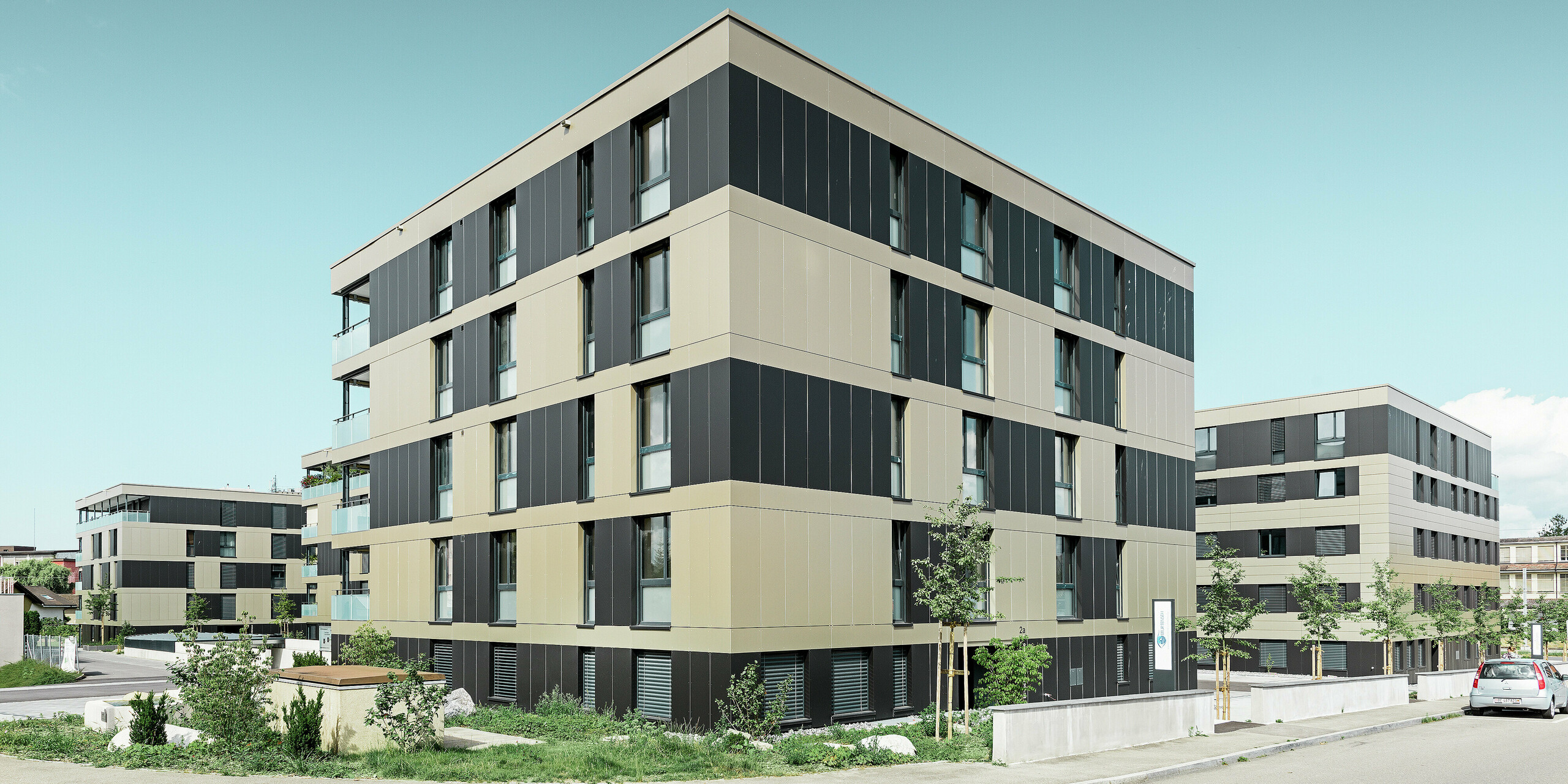 Die moderne Architektur dieser Wohnanlage in Murten (CH) wird durch die PREFA Fassade mit Aluminium Verbundplatten in Bronze und Schwarzgrau unterstrichen. Die langlebige und pflegeleichte Oberfläche schützt das Gebäude nicht nur vor Umwelteinflüssen, sondern verleiht dem gesamten Baukörper ein elegantes und zeitloses Design.