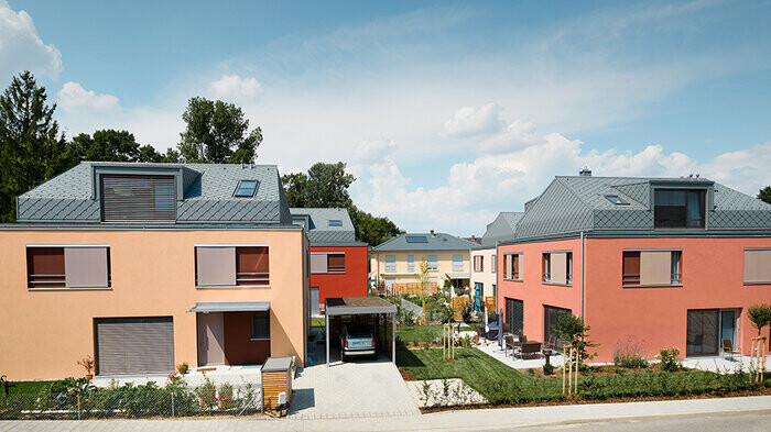 Complesso residenziale multifamiliare con facciate in toni rossi e tetti a scaglie in alluminio in grigio chiaro di PREFA