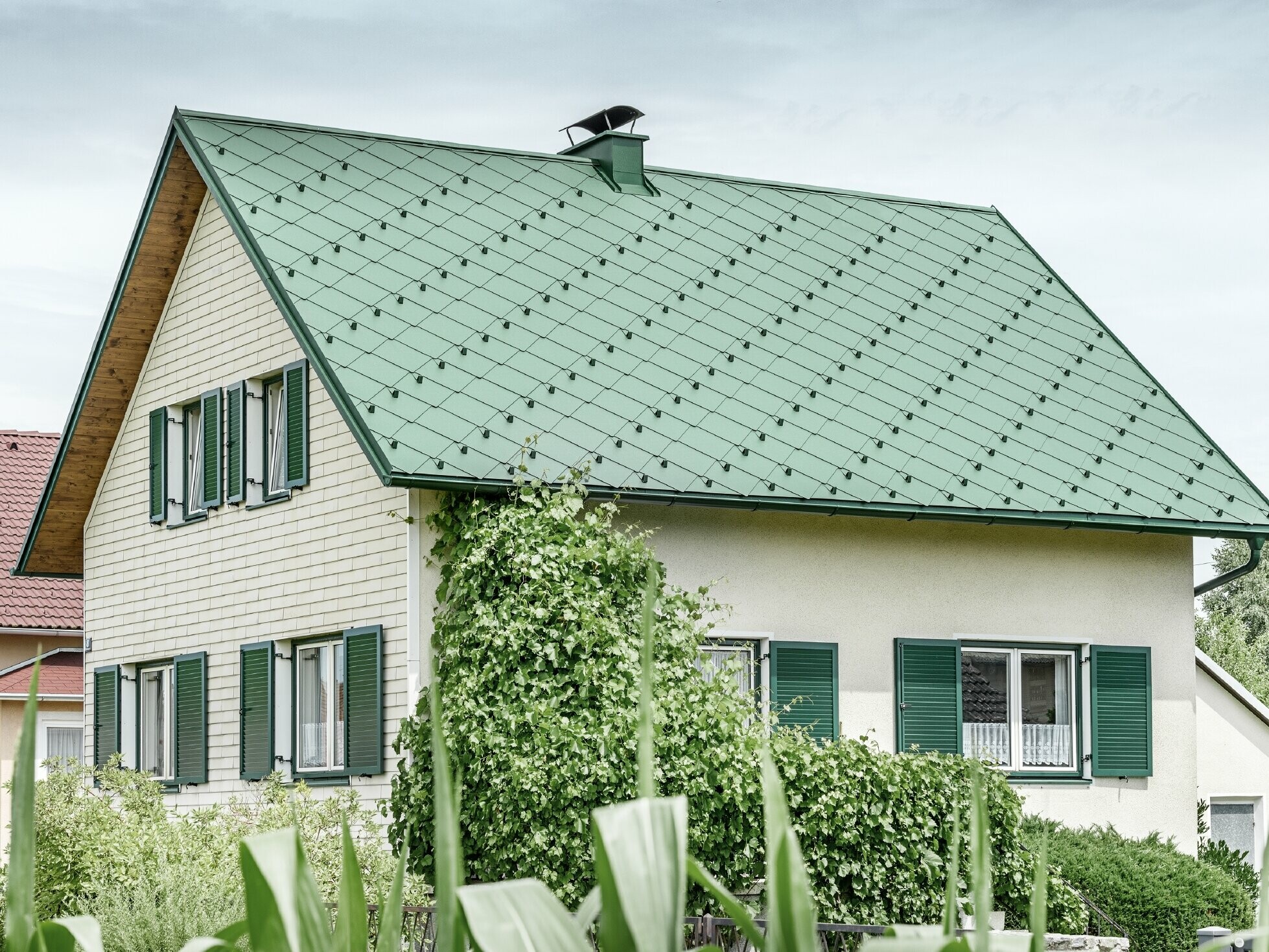Casa unifamiliare classica con tetto a due falde con copertura in alluminio di colore verde muschio e persiane verdi