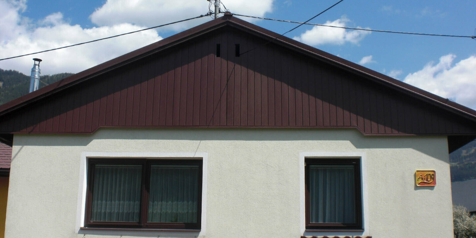 Ristrutturazione della facciata del timpano con doghe di rivestimento PREFA marroni, facciata verde chiaro
