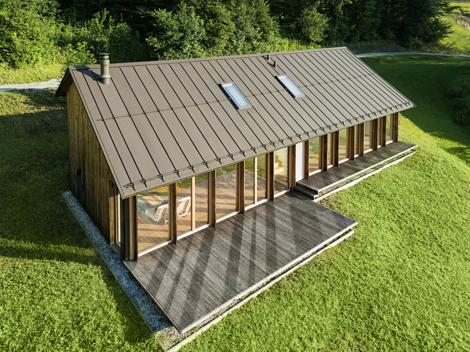 Modernes Holzhaus mit großzügiger Glasfassade und strapazierfähigem PREFALZ Aluminiumdach in P.10 Braun – ideal für Hanglagen wie in Vinje. Die hochwertige Dacheindeckung sorgt für maximale Wetterbeständigkeit, lange Lebensdauer und eine elegante Optik. Durch präzise Verlegung der Stehfalze und integrierte Dachfenster entsteht ein lichtdurchflutetes, nachhaltiges Wohnkonzept. Die Vogelperspektive zeigt die präzise Verarbeitung der Stehfalze aus Aluminium.