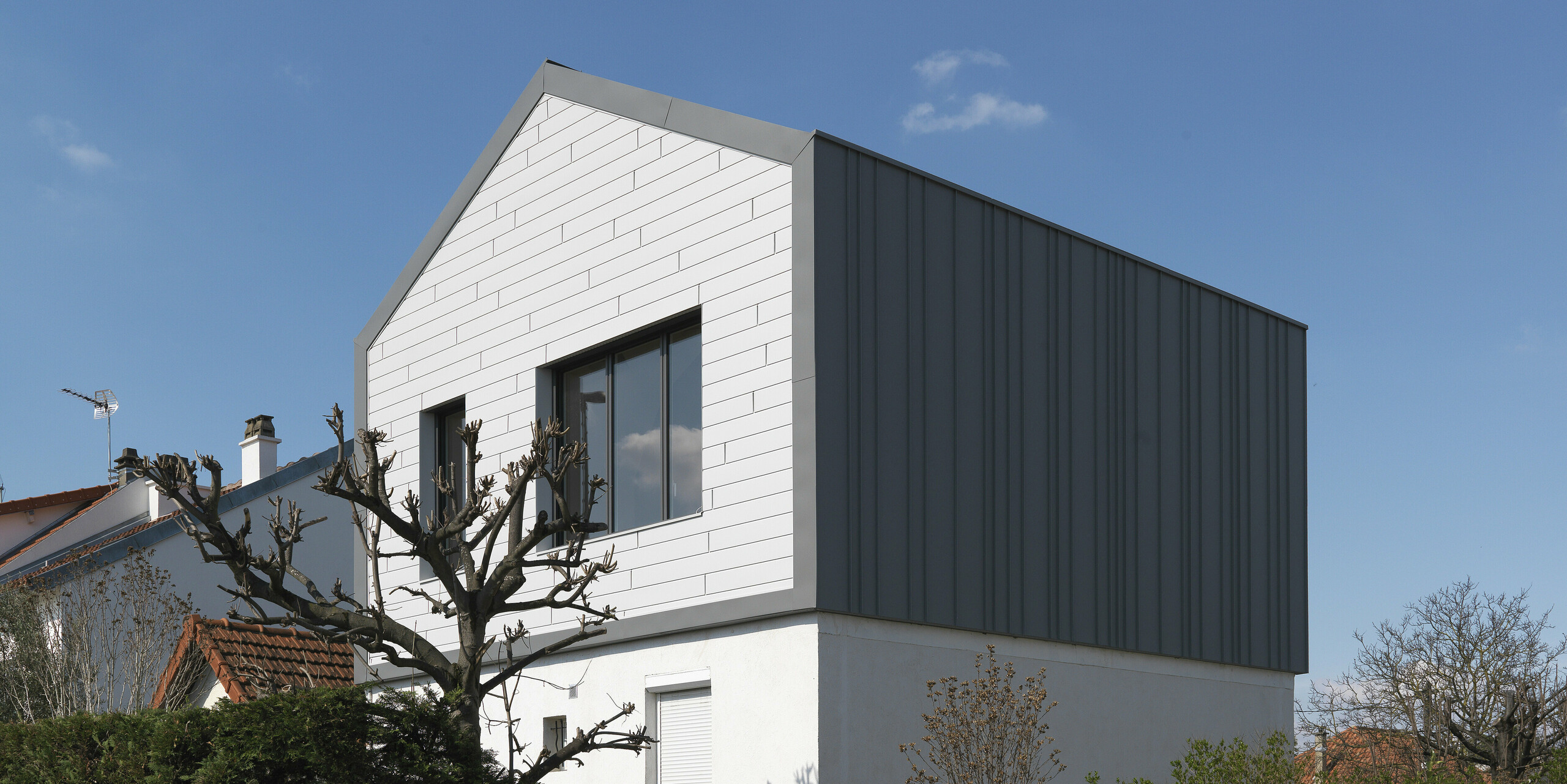 Vue sur la rue d'une maison familiale à Houilles (France). Pour le bâtiment, les Siding PREFA en P.10 blanc pur ont été combinés en façade et PREFALZ en P.10 gris souris en toiture et façade.