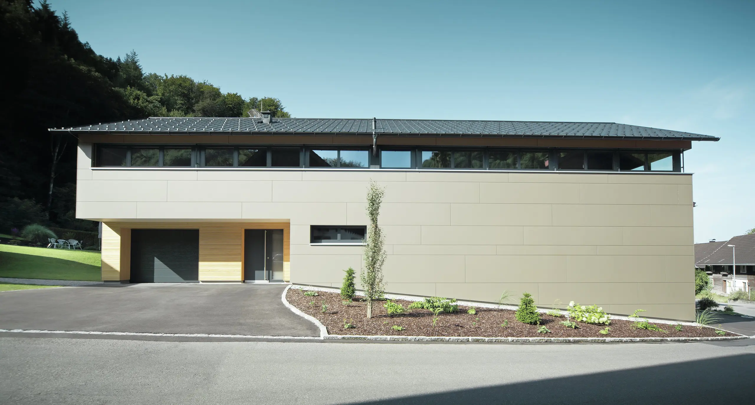 Casa lunga con pannello di copertura PREFA in P.10 antracite, combinato con pannello composito PREFA in bronzo sulla facciata; stile di costruzione moderno combinato con finestre strette e facciata in legno