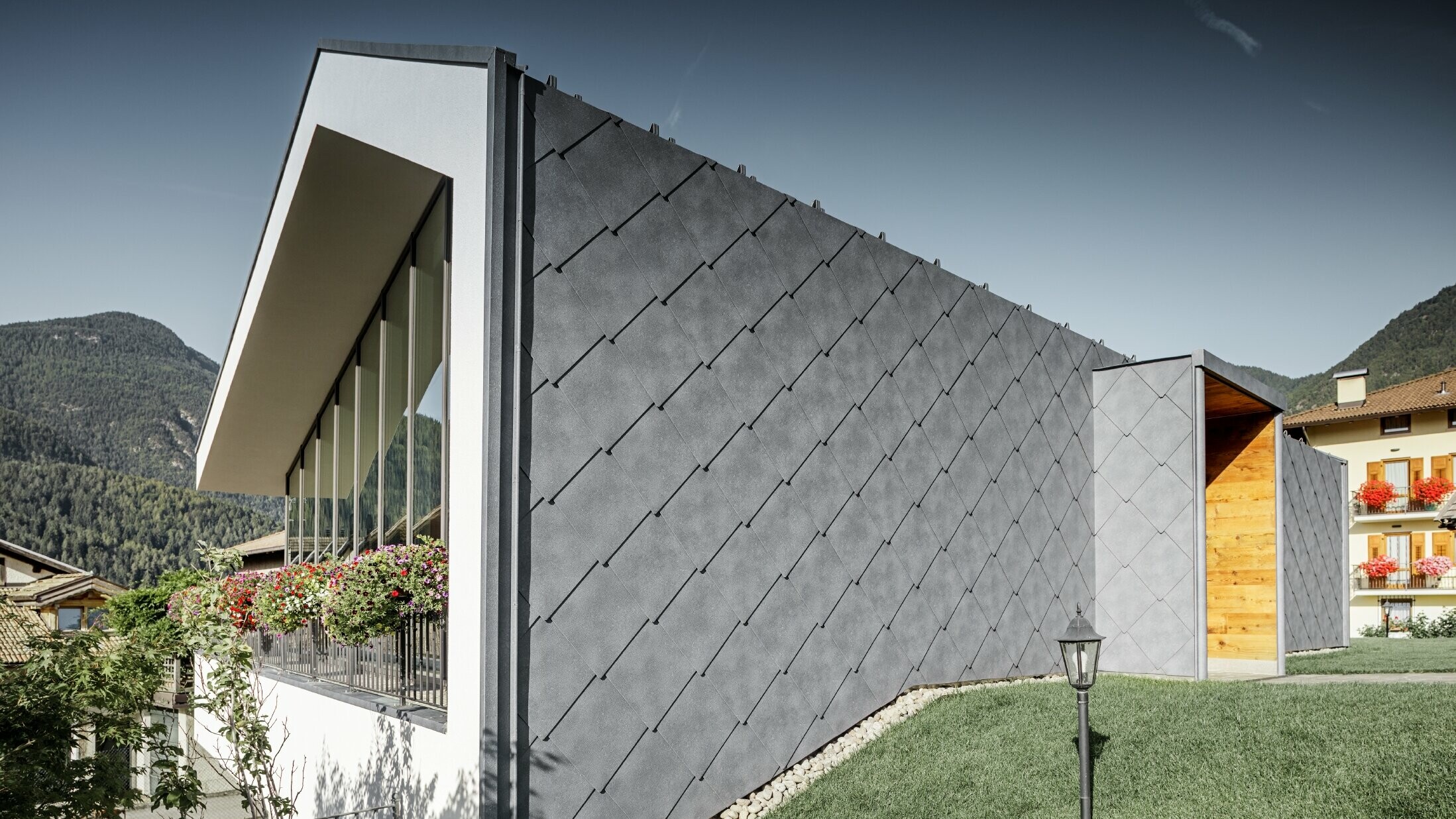 Moderno salone da parrucchiere a Livo rivestito con scaglia 44 di copertura e per facciata in grigio pietra di PREFA