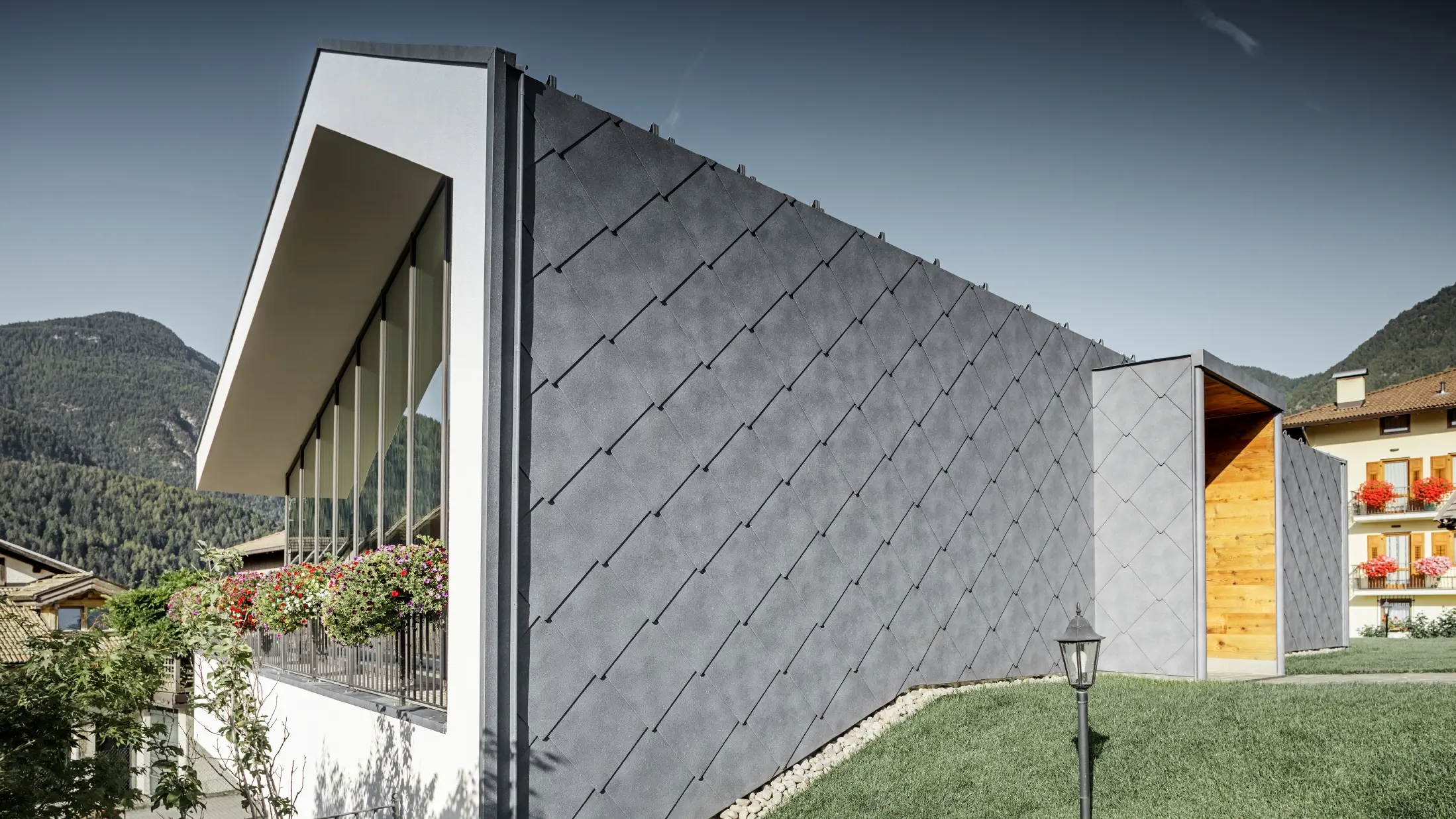 Moderno salone da parrucchiere a Livo rivestito con scaglia 44 di copertura e per facciata in grigio pietra di PREFA