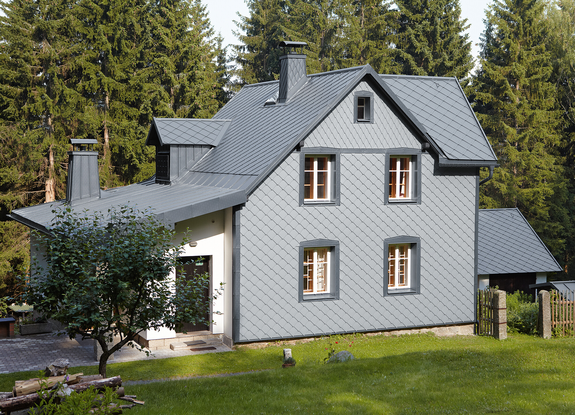 Fassade mit PREFA Wandraute 29 × 29 in Hellgrau auf der Wetterseite Einfamilienhaus in Waldlage mit witterungsbeständiger PREFA Aluminiumfassade in Hellgrau.