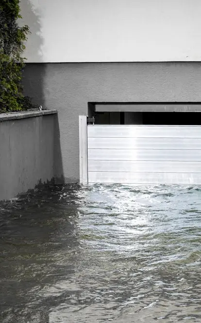 Garageneinfahrt in den Keller mit einem Garagentor das geschützt wird durch den PREFA Hochwasserschutz. Die Einfahrt ist voller Wasser.
