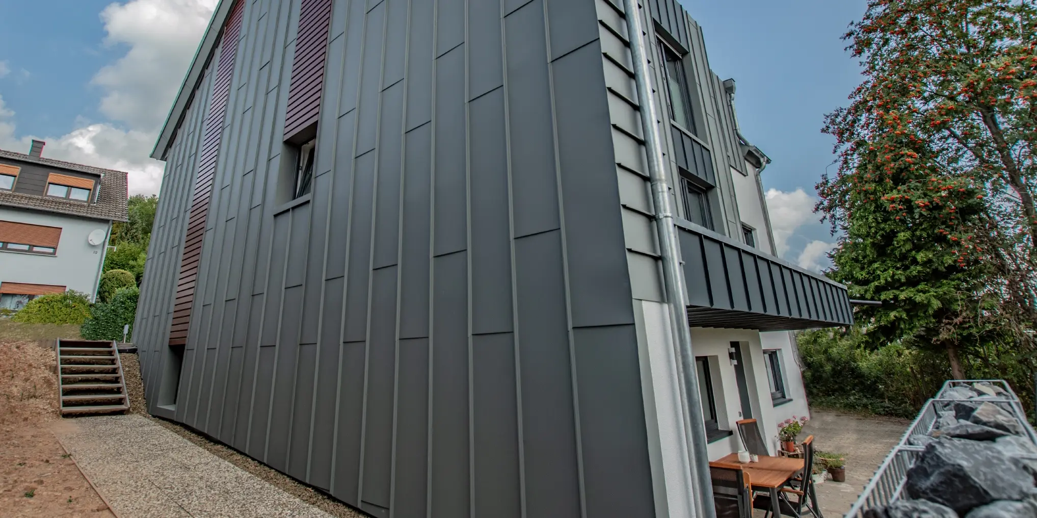 Conception de façade avec façade à agrafage angulaire vertical en gris souris et panneaux de façade posés à l’horizontale, couleur bois foncé. Toute la façade a été réalisée en aluminium par PREFA.