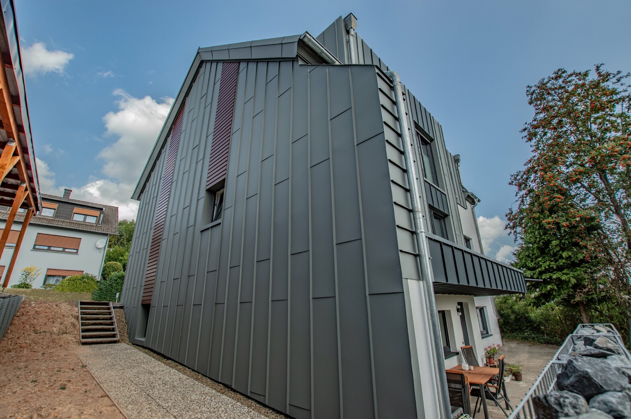 Conception de façade avec façade à agrafage angulaire vertical en gris souris et panneaux de façade posés à l’horizontale, couleur bois foncé. Toute la façade a été réalisée en aluminium par PREFA.