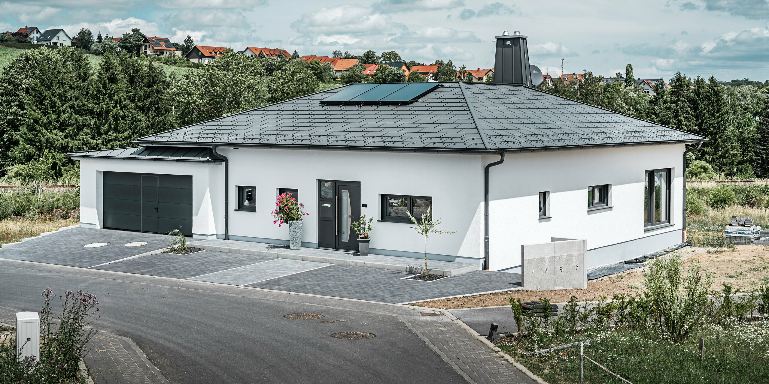 R.16 PREFA et joint debout PREFALZ ainsi que tuyau de descente et gouttière suspendue en P.10 gris sombre sur le toit d'un bungalow. 