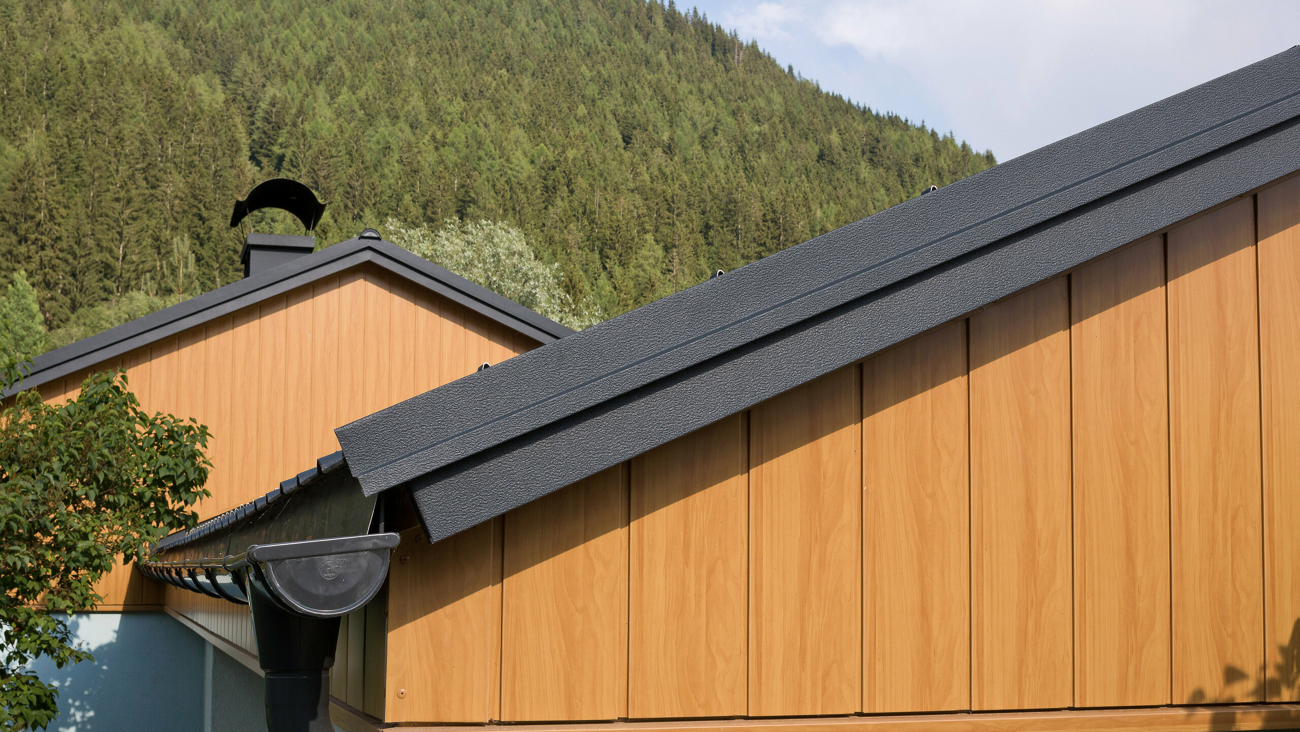 Rivestimento di timpano con le doghe di rivestimento in alluminio di PREFA di colore rovere naturale, montante in diagonale con grondaia PREFA in antracite.