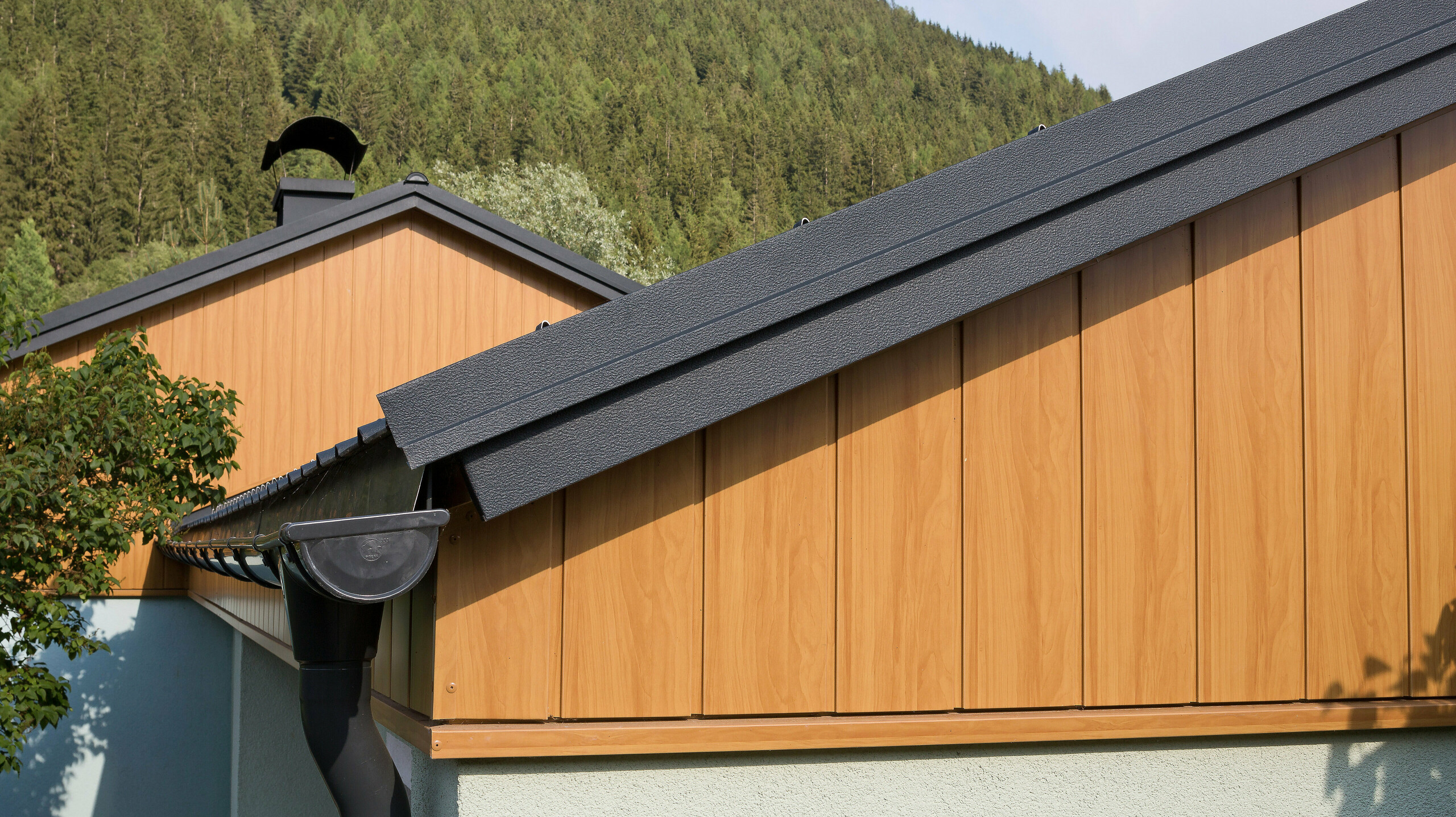 Revêtement de pignon avec les Sidings en aluminium de PREFA couleur chêne naturel montés à la verticale avec une gouttière PREFA anthracite.