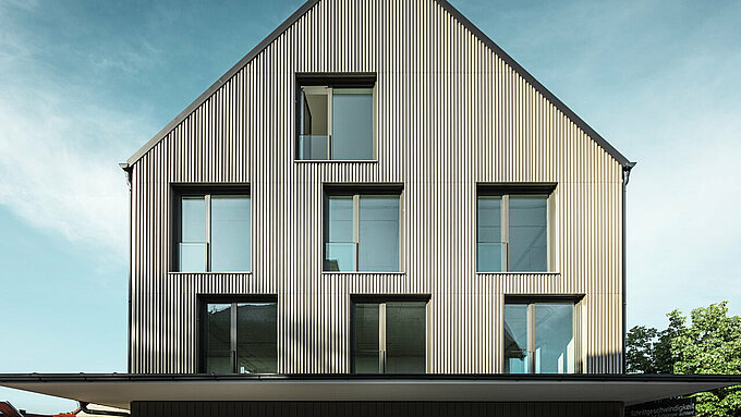 Das Bild zeigt ein modernes Gebäude in Feldkirch, entworfen vom Architekten Stefan Heigl. Die Fassade ist mit Prefalz in der Farbe Bronze verkleidet, während das Satteldach mit Prefalz in Schwarzgrau gedeckt ist. Große, rechteckige Fenster sorgen für viel Tageslicht im Inneren. Das Gebäude kombiniert hochwertige Materialien und eine elegante Architektur, die sowohl funktional als auch ästhetisch ansprechend ist. Diese moderne Bauweise und die Verwendung von Prefalz Materialien verleihen dem Gebäude ein zeitgemäßes und stilvolles Erscheinungsbild.
