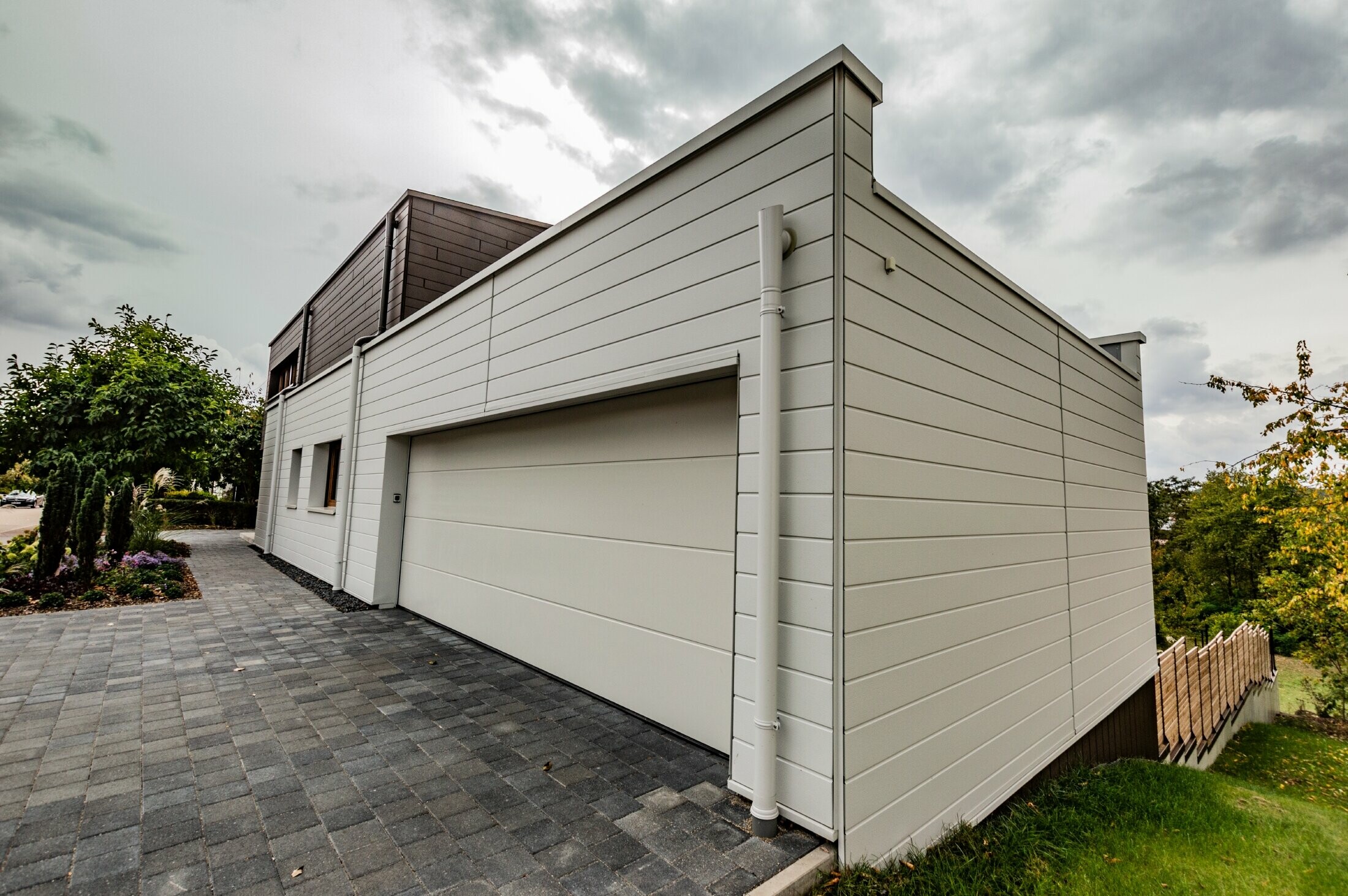 Rivestimento del garage con doga PREFA in bianco posata orizzontalmente con grondaia con sbocco PREFA.