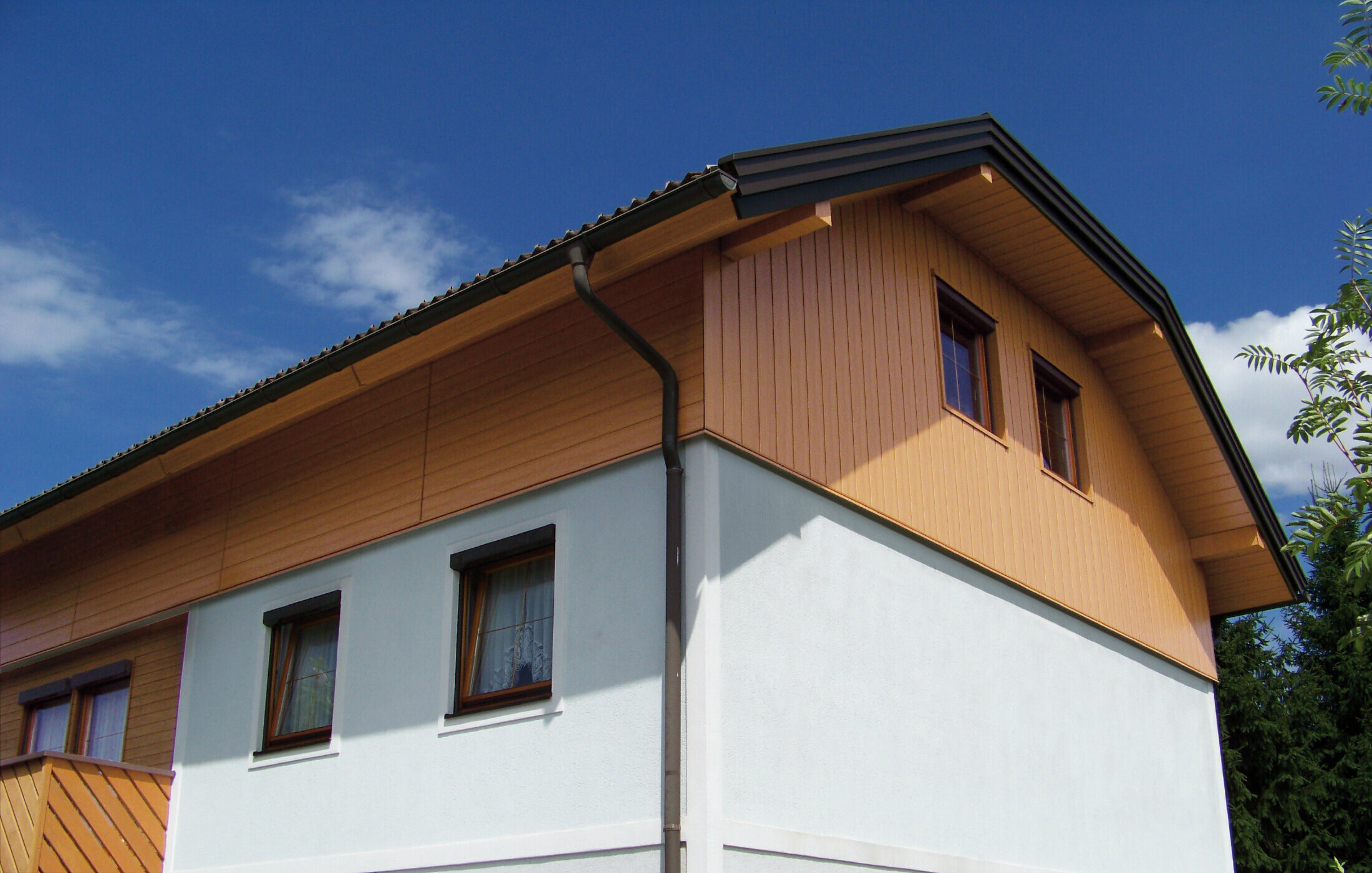Casa unifamiliare di grandi dimensioni con tetto a due spioventi con falda a timpano e rivestimento del timpano con doghe di rivestimento PREFA con effetto legno chiaro