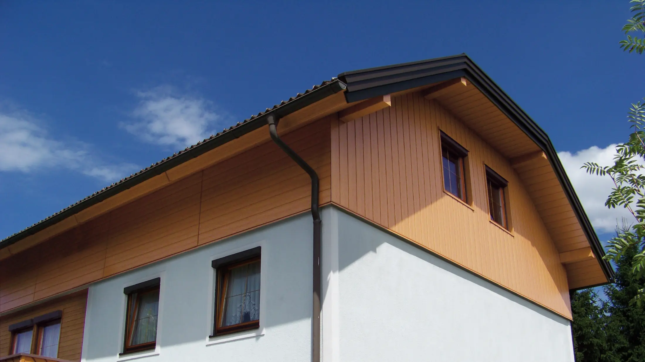 Casa unifamiliare di grandi dimensioni con tetto a due spioventi con falda a timpano e rivestimento del timpano con doghe di rivestimento PREFA con effetto legno chiaro