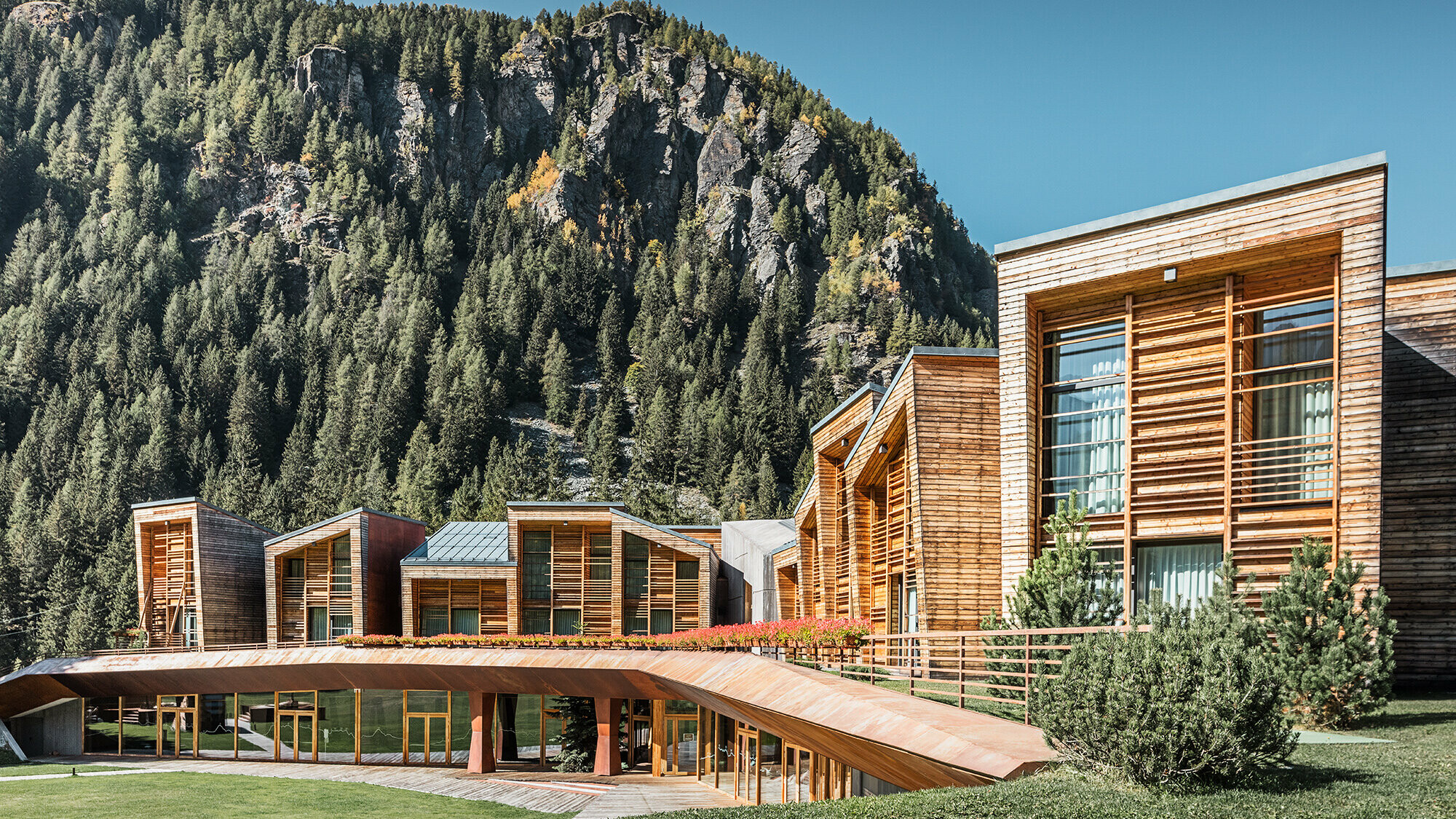 Seitenansicht des oberen und unteren Bereichs des CampZero Resorts im Aostatal mit Gebirge im Hintergrund.