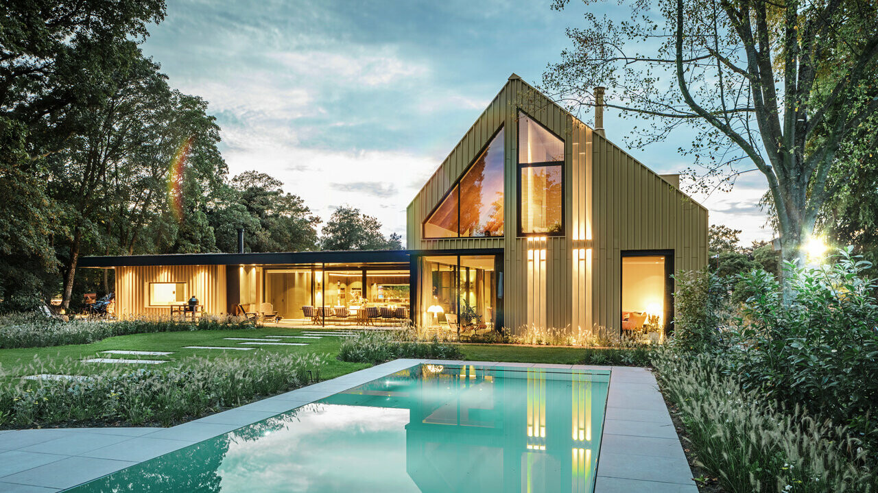 Vue de la maison individuelle d'Elst recouverte en Prefalz et Falzonal. La maison est entourée d'arbres et une piscine est visible au premier plan.