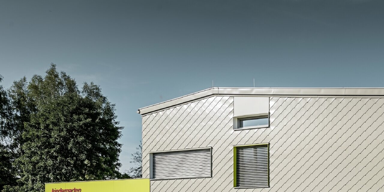 Le jardin d’enfants a été partiellement habillé avec le losange de façade 29 PREFA couleur bronze. Cette partie du bâtiment ne présente pas d’avancée de toit. Le reste de la façade a été habillé de panneaux de façade couleur jaune.