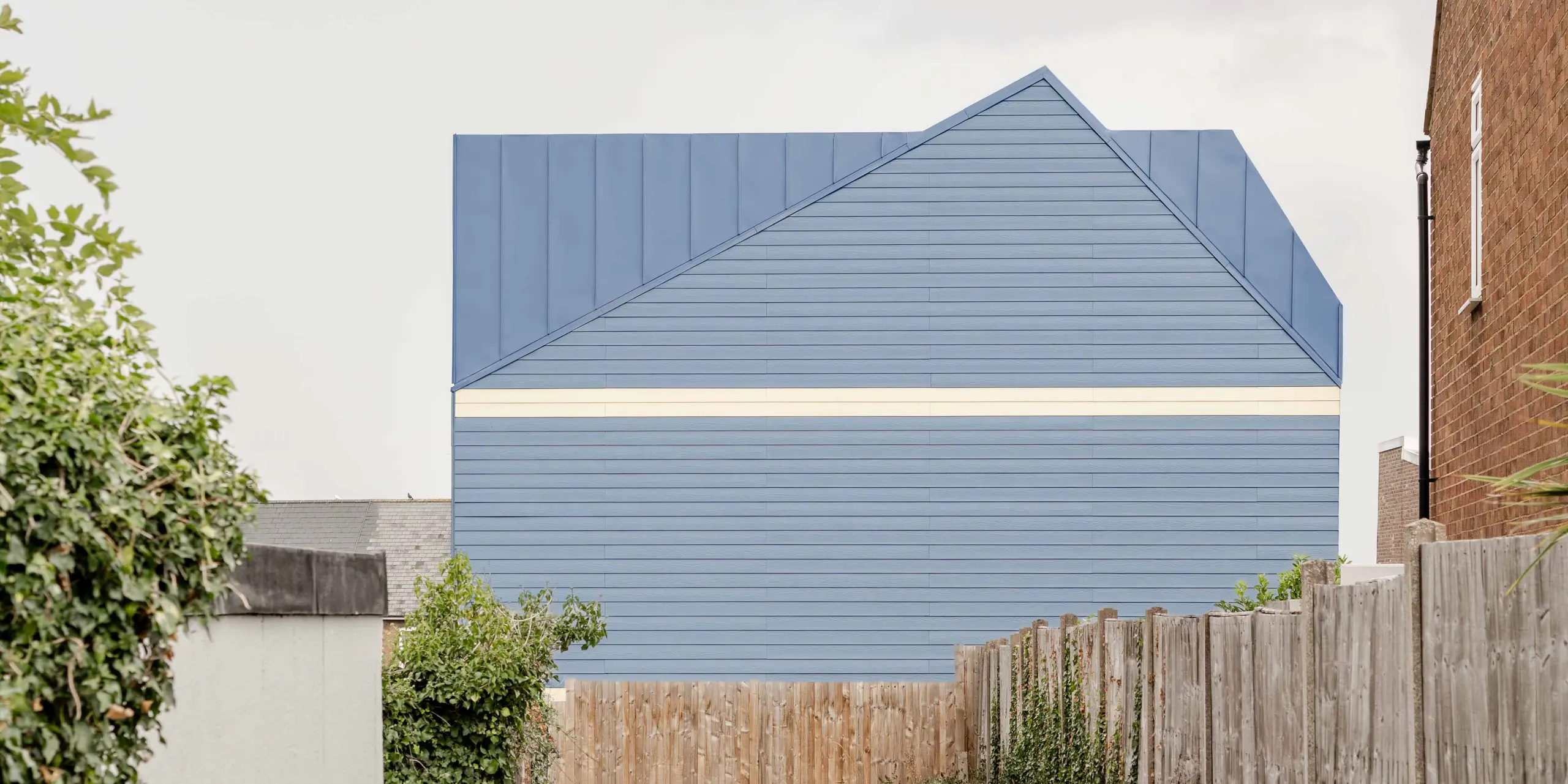 La photographie révèle la façade remarquable d'une maison mitoyenne de Goldsmith-Mews, revêtue d'aluminium PREFA FALZONAL bleu pigeon. La pureté des lignes des joints verticaux et horizontaux crée une façade géométrique affirmée qui se distingue nettement des bâtiments environnants. Le contraste avec les parties basses claires de la façade renforce la modernité et la précision du design. Durable et inaltérable, l'aluminium PREFA offre une excellente protection contre les intempéries et garantit un aspect haut de gamme et durable, conférant à l'ensemble une identité unique.
