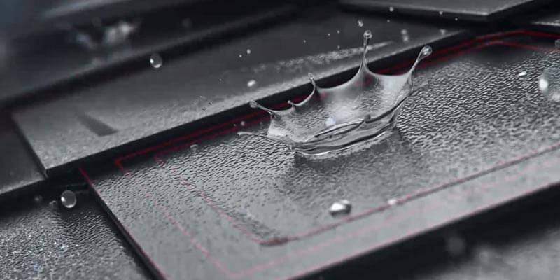 Nahaufnahme der PREFA Dachraute mit einem großen Wassertropfen auf der Oberläche. Man erkennt gut die Struktur der Stucco Oberfläche. Die Dachraute ist in der Farbe anthrazit.